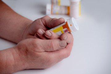 rugged working hands of a man holding pain medication prescription bottle on white. shallow depth of field