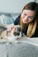 Cute girl cuddling with calico cat on bed in apartment, copy space, sweet