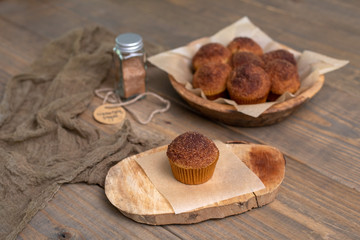 Naklejka premium Homemade Muffins topped with Cinnamon Sugar in Rustic Setting; Wooden Bowl, Wooden Table, Cinnamon Sugar Jar in Background