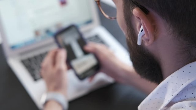 Handsome man using smartphone scrolling social network. Freelancer workspace. Male office worker browsing web site. Hand scrolling pictures, photos in application. Screen is blurred. Close up