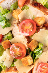 Caesar salad texture. Slices of chicken breast, green lettuce, Parmesan cheese, croutons, and cherry tomatoes, shot from the top with the typical dressing