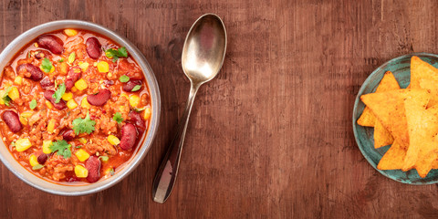 A panorama of chili con carne with nachos, shot from the top on a dark rustic wooden background with a place for text, a Mexican food design template for a banner or flyer