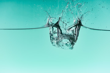 transparent ice cubes falling in water with splash on turquoise background