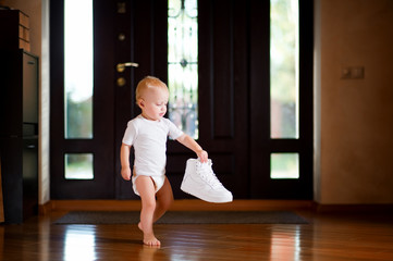 little girl holding a white sneaker standing in the hallway at home