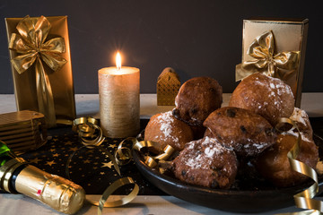 Oil dumplings (oliebollen) on black plate, with champagne,golden candle and gifts. Traditional treat on New Years Eve in The Netherlands