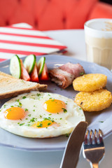 Traditional british breakfast with fried egg, wheat crunchy toasts, potato hash browns, bacon and salad
