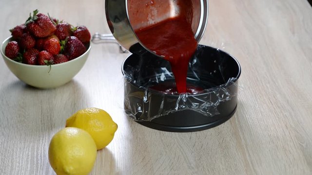 A woman pours strawberries jelly into a mold to make jelly filling for cake.