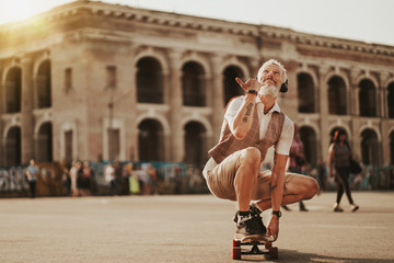 Happy man in white shirt ride on skateboard near road on street background. Outdoors portrait of stylish guy. Urban lifestyle