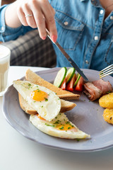 Woman is having traditional british breakfast with fried egg, wheat crunchy toasts, potato hash browns, bacon and salad