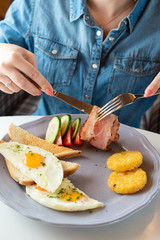Woman is having traditional british breakfast with fried egg, wheat crunchy toasts, potato hash browns, bacon and salad
