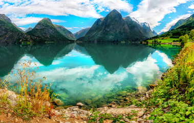 Norwegian landscape with Reflections in the calm water of the Norwegian crystal clear lake with a rocky bottom and green mountains. Oppstryn, Norway.