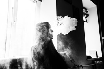 Vaping teenager. Young pretty white girl smoking an electronic cigarette opposite the window  in vape bar. Bad habit. Black and white.