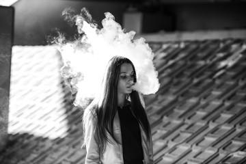 Vape teenager. Young cute girl in  casual clothes smokes an electronic cigarette outdoors in summer...