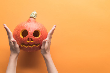 cropped view of woman holding carved spooky Halloween pumpkin on orange background