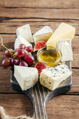 Various cheese, honey, grapes and figs on a wooden cutting board