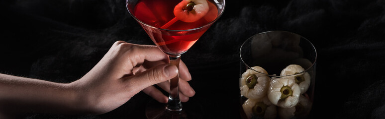 panoramic shot of woman holding red Halloween cocktail in black clouds