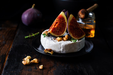 Camembert cheese with figs, walnuts, honey and thyme served for a dinner in dark key. Selective focus.