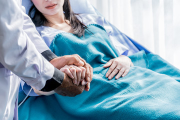 Male doctor holding female patient hand on the hospital bed.