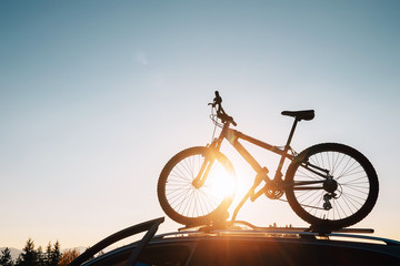 Fototapeta na wymiar Mounted mountain bicycle silhouette on the car roof with evening sun light rays background. Safe sport items transportation using a car concept image.