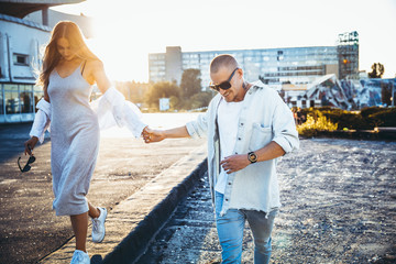 Tanned young caucasian couple, modern lovestory in film grain effect and vintage style. Sunset. Walking on the city's street, confident and happy, summer. Honeymoon concept. Toned in teal orange.