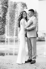 Photo of an elegant woman in a white dress hugging her lover. Young couple in love together in summer. Young lovers during their romantic date. Cheerful couple hugging and kissing. Black and white