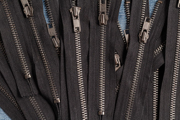 Pack a lot of black metal antique zippers stripes with sliders pattern for handmade sewing tailoring haberdashery leather craft on the blue denim background