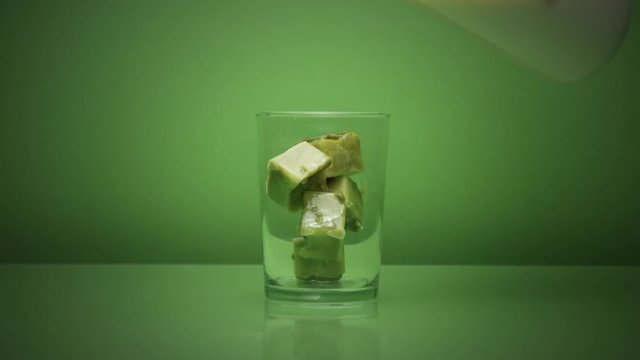 glass on green with matcha tea ice cubes and milk pouring in it. 