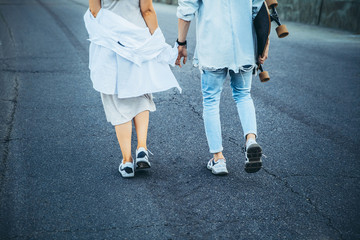 Tanned young caucasian couple, modern lovestory in film grain effect and vintage style. Sunset. Walking on the city's street with longboard, summer evening. Honeymoon concept. Toned in teal orange.