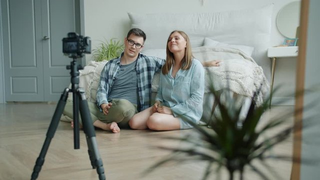 Girl and guy vloggers are recoding video for online vlog showing thumbs-up talking sitting on bedroom floor at home. Lifestyle and occupation concept.