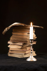 Candle with flame on the background of the stack of books