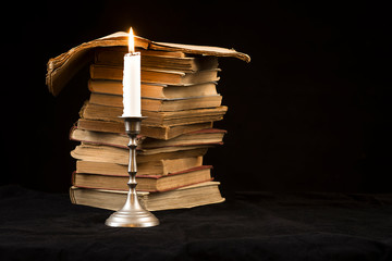 Candle with flame on the background of the stack of books