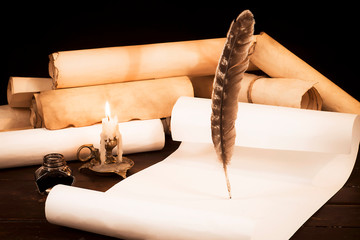 A lit candle and quill with inkwell against a background of a scroll of parchment