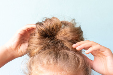The girl straightens the disheveled bun on her head with her hands. Modern fast hairstyle. Blue...