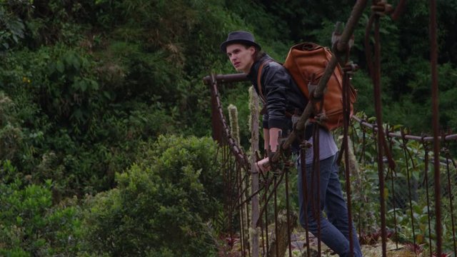 Travel and Adventure - Young man crossing a decrepit old suspension bridge