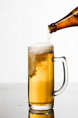 beer pouring from bottle into glass with bubbles isolated on white