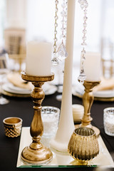 Naklejka premium Tall golden candlesticks with white candles decorate the table at the event