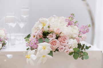 Elegant small bouquet of roses, greens and other colours on a white wedding table