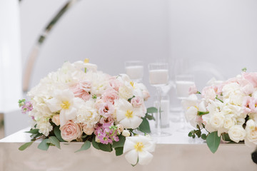 Stylish decoration of the modern wedding table with white candles and flowers in light shades.