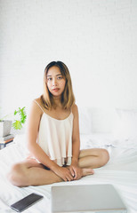 beautiful woman working on a laptop sitting on the bed in the house.