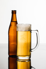 glass of beer with foam near wet bottle isolated on white