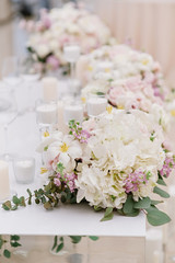 Stylish decoration of the modern wedding table with white candles and flowers in light shades.