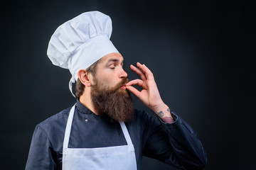 Male chef in uniform. Cook with taste approval gesture. Bearded chef, cook, baker gesturing excellent. Chef in white hat and apron with perfect sign. Professional chef man showing sign for delicious.
