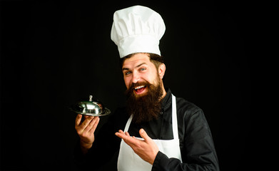 Chef cook holds metallic dish. Serving and presentation. Cook holds cloche in restaurant. Cooking. Restaurant serving. Presentation. Male chef presenting silver tray. Bearded chef holds food tray.