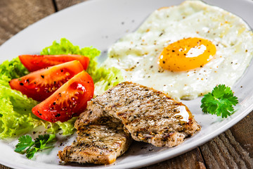 Grilled steaks with fried egg and vegetables on white plate