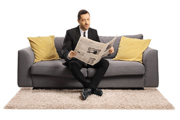 Young businessman sitting on a sofa and reading a newspaper