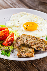 Grilled steaks with fried egg and vegetables on white plate