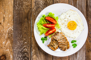 Grilled steaks with fried egg and vegetables on white plate