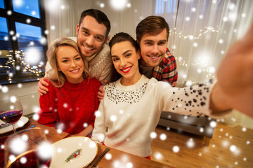 Obraz na płótnie Canvas holidays and celebration concept - happy friends taking selfie at home christmas dinner over snow