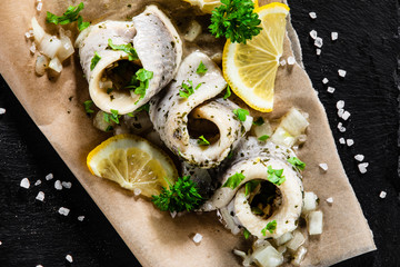 Marinated herring fillets on piece of paper on black stone