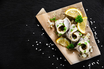 Marinated herring fillets on piece of paper on black stone